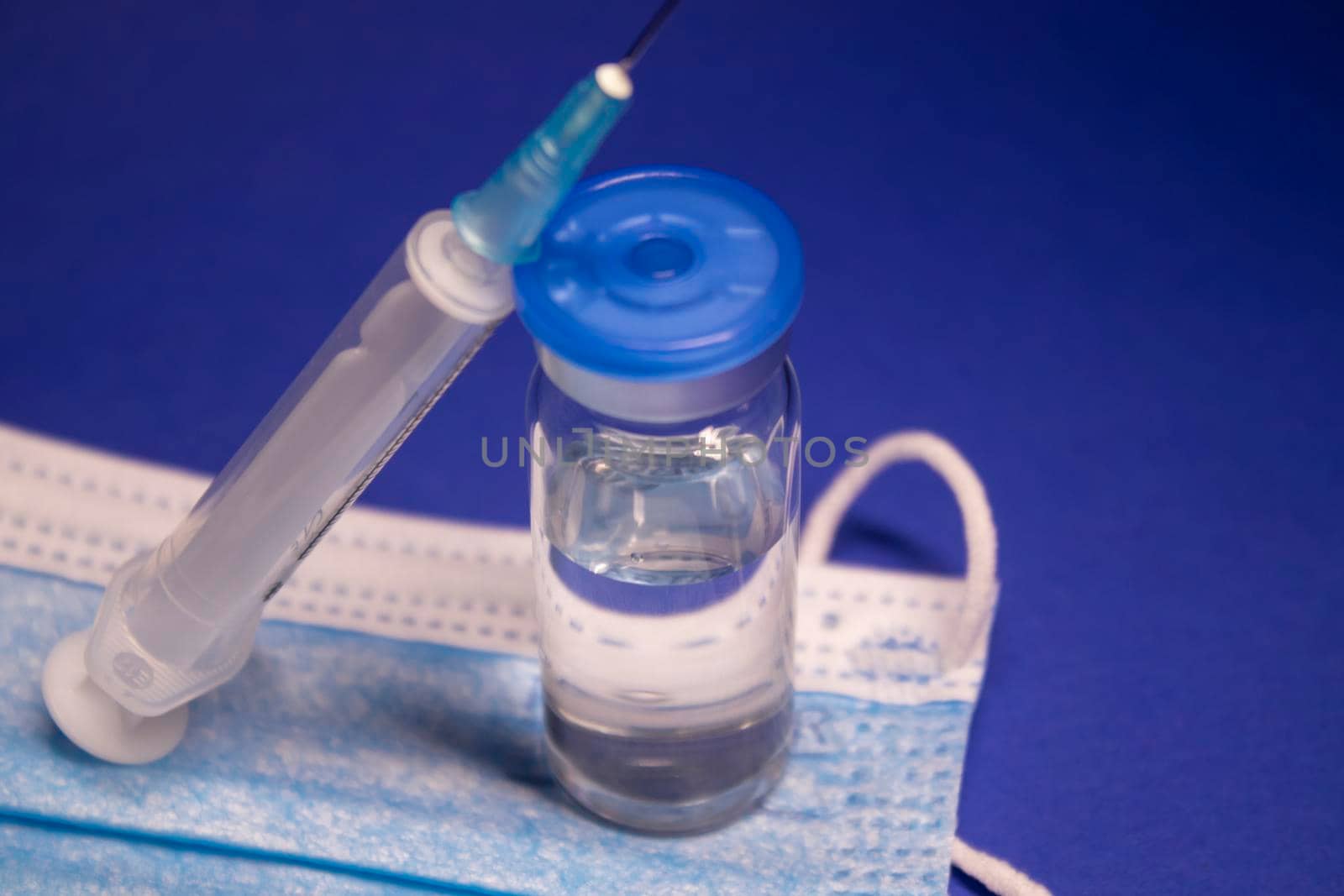 Vaccine bottle phial with no label on blue medical mask and medical syringe with injection needle. isolated on blue background. cure. Development of coronavirus vaccine COVID-19. copy space