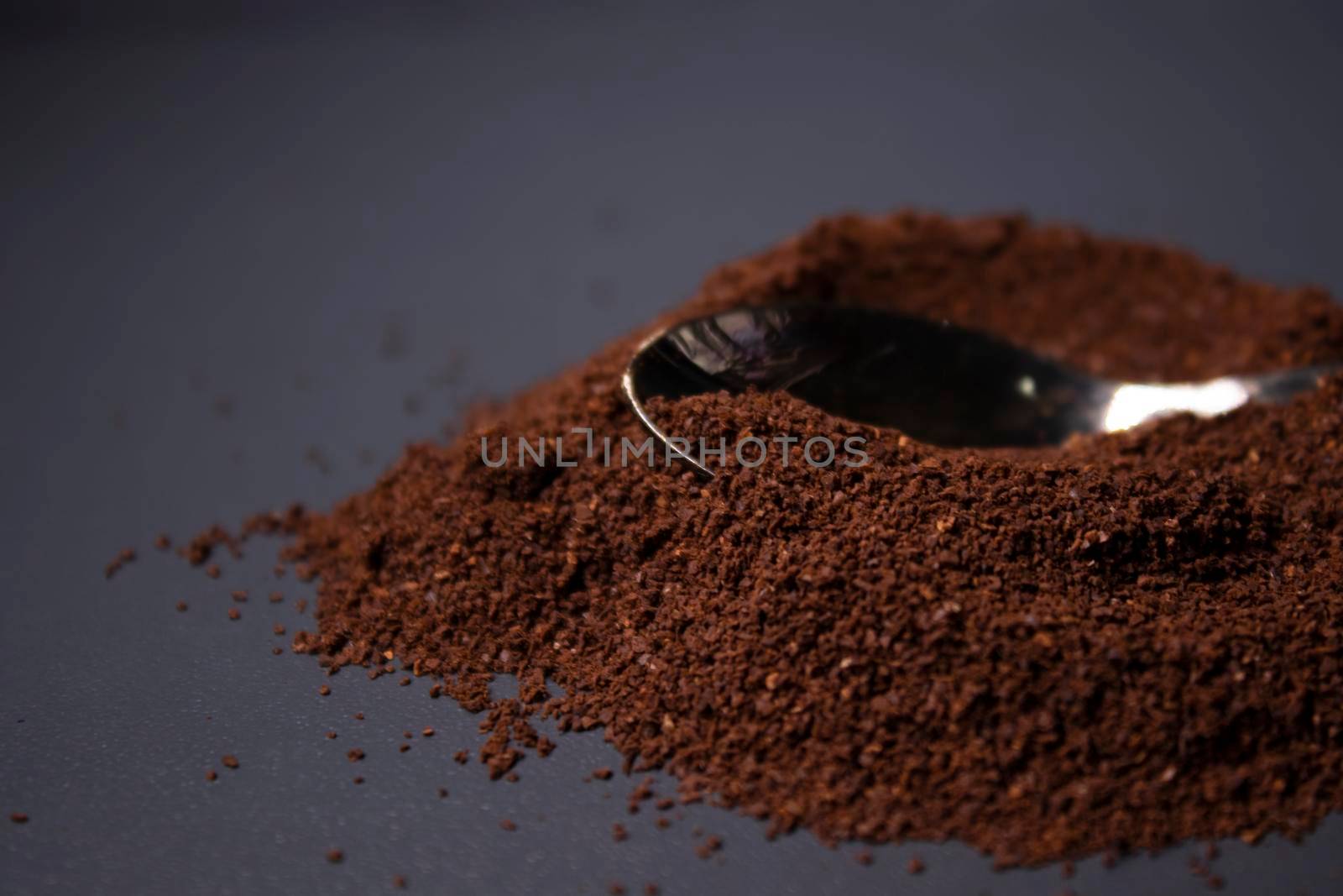 gold teaspoon in a pile of ground or instant coffee on dark background.