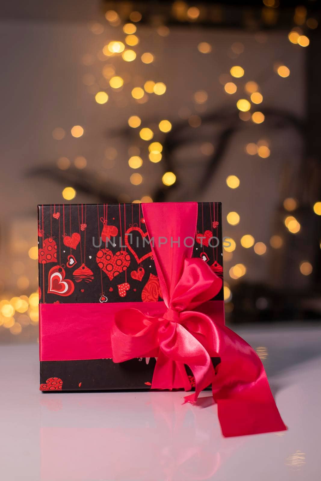 black with hearts gift box with pink ribbon bow on gold bokeh background.