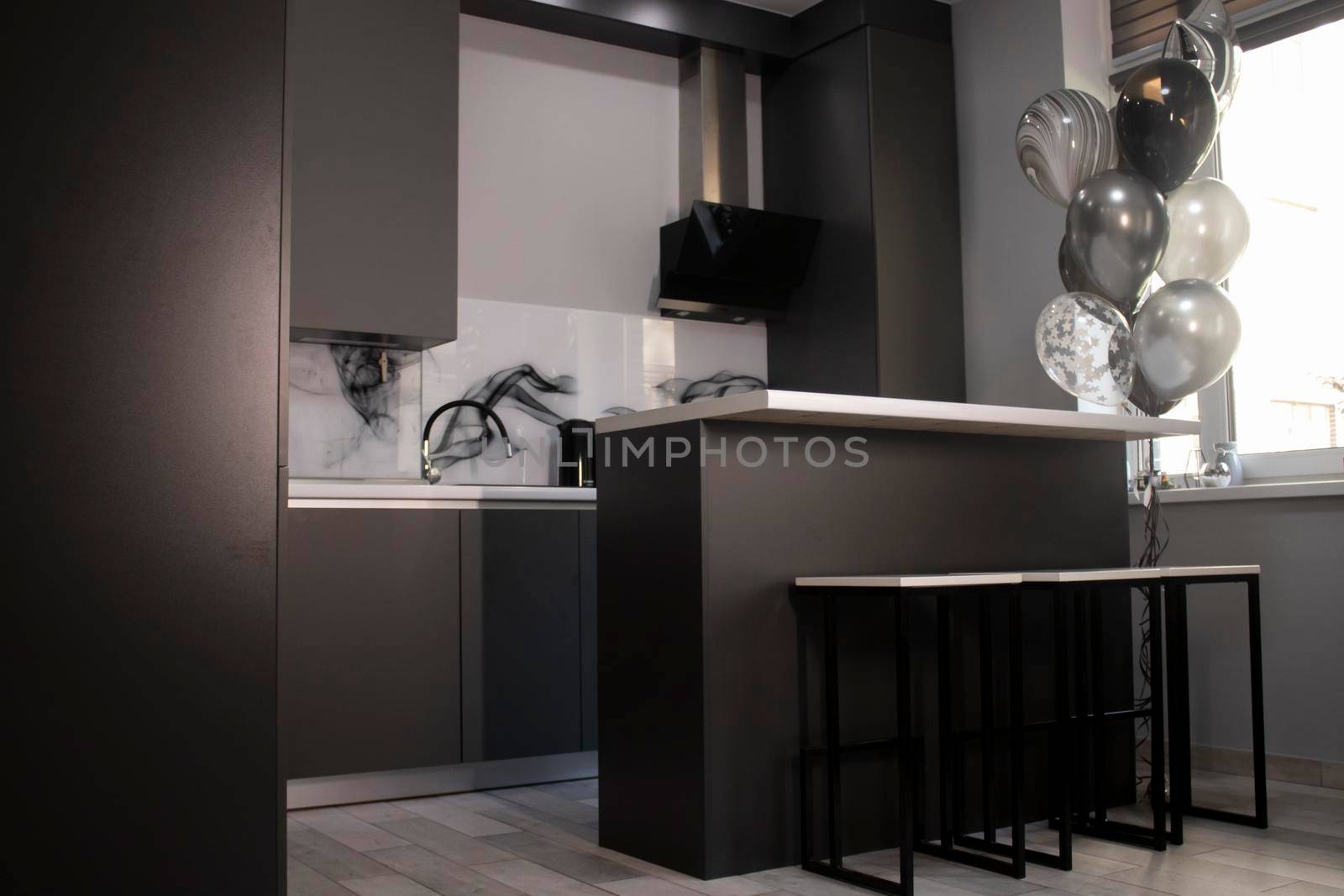 Corner of stylish Minimalistic grey kitchen, dark gray cupboards, white countertops and bar with stools. black and white balloons. High quality photo