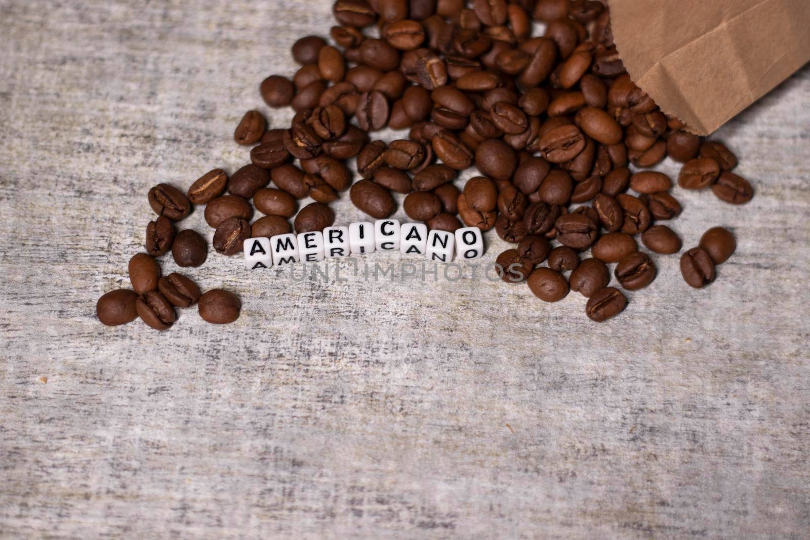 close up of Freshly roasted coffee beans near word AMERICANO written with little white cubes. top view.