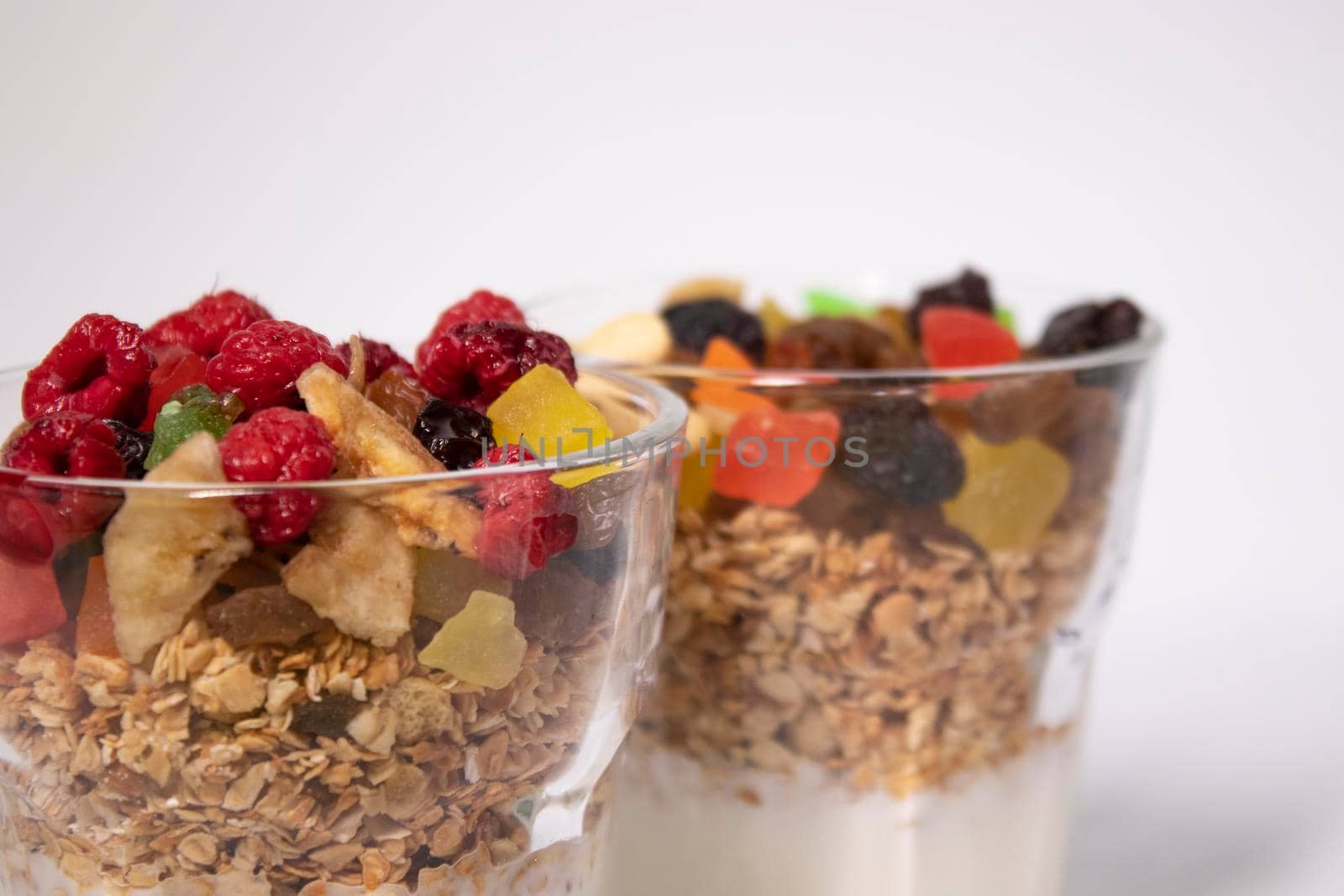 muesli dessert with yogurt and candied or dried fruits with raspberries on top in glass isolated on white background. breakfast Granola