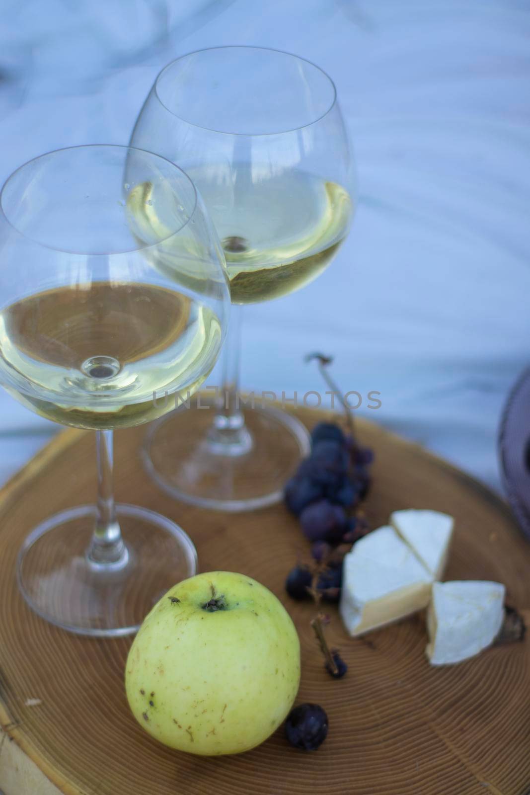 wooden stand with two glasses of champagne, grapes and camembert cheese on a white blanket in the field. picnic.