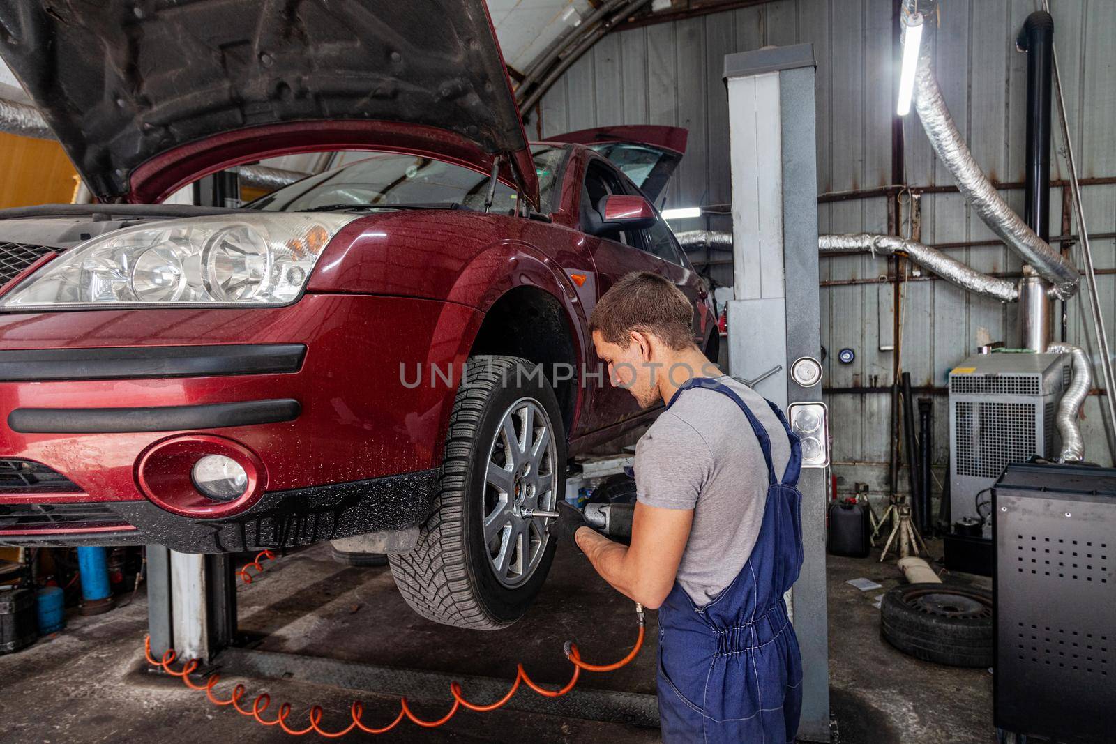 A mechanic is maintaining wheels on a vehicle in auto garage with pneumatic tool.