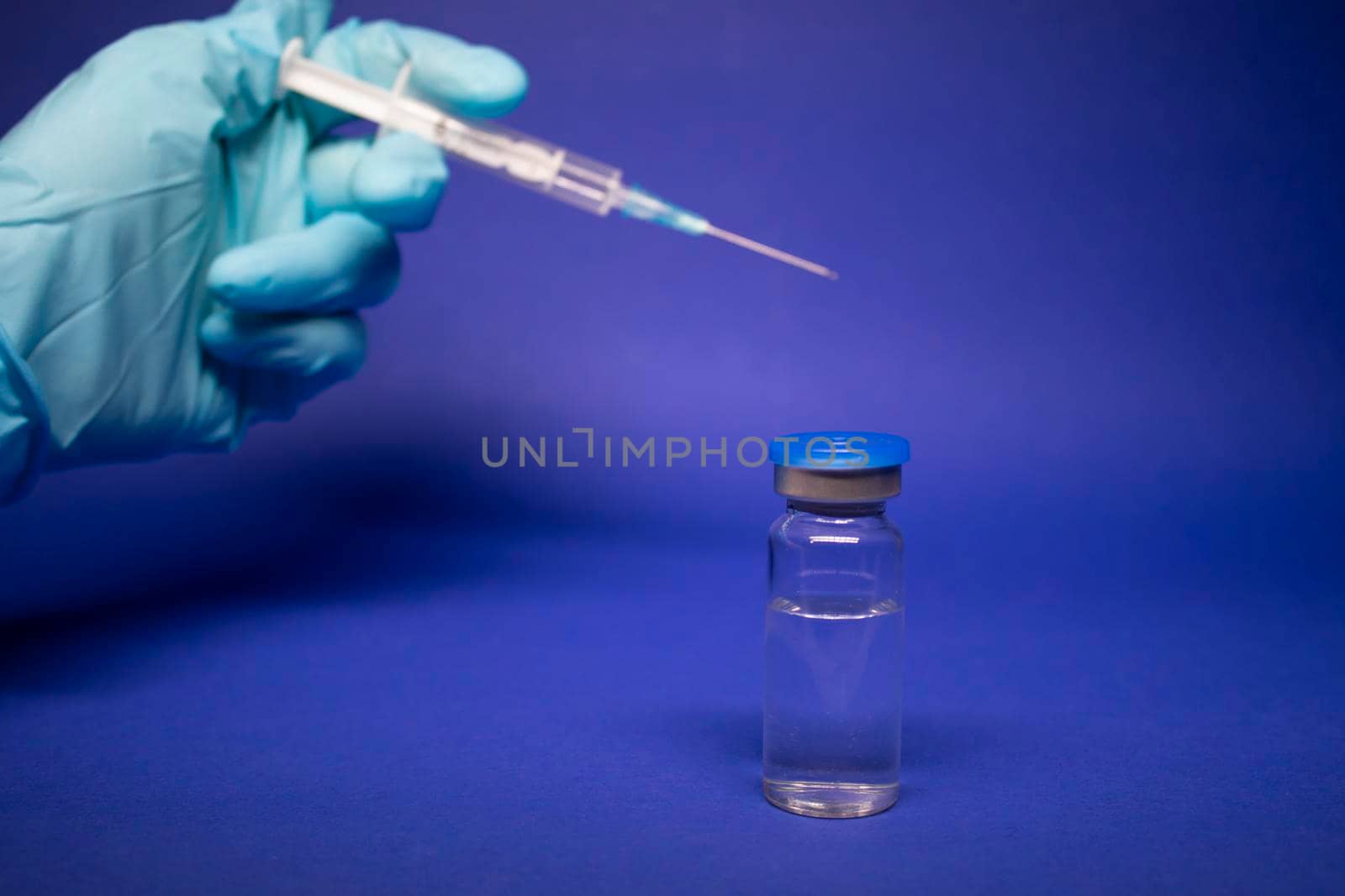 Development of coronavirus vaccine COVID-19. medical syringe with injection needle in blue medical glove near bottle phial with no label. isolated on blue background. cure. copy space