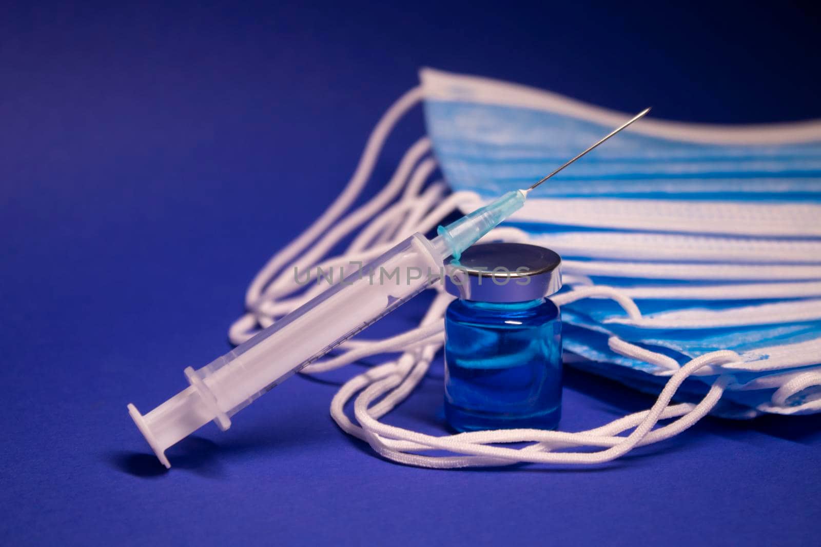 Vaccine bottle phial with no label and medical syringe with injection needle near pile of blue medical masks . isolated on blue background. cure. Development of coronavirus vaccine COVID19. copy space