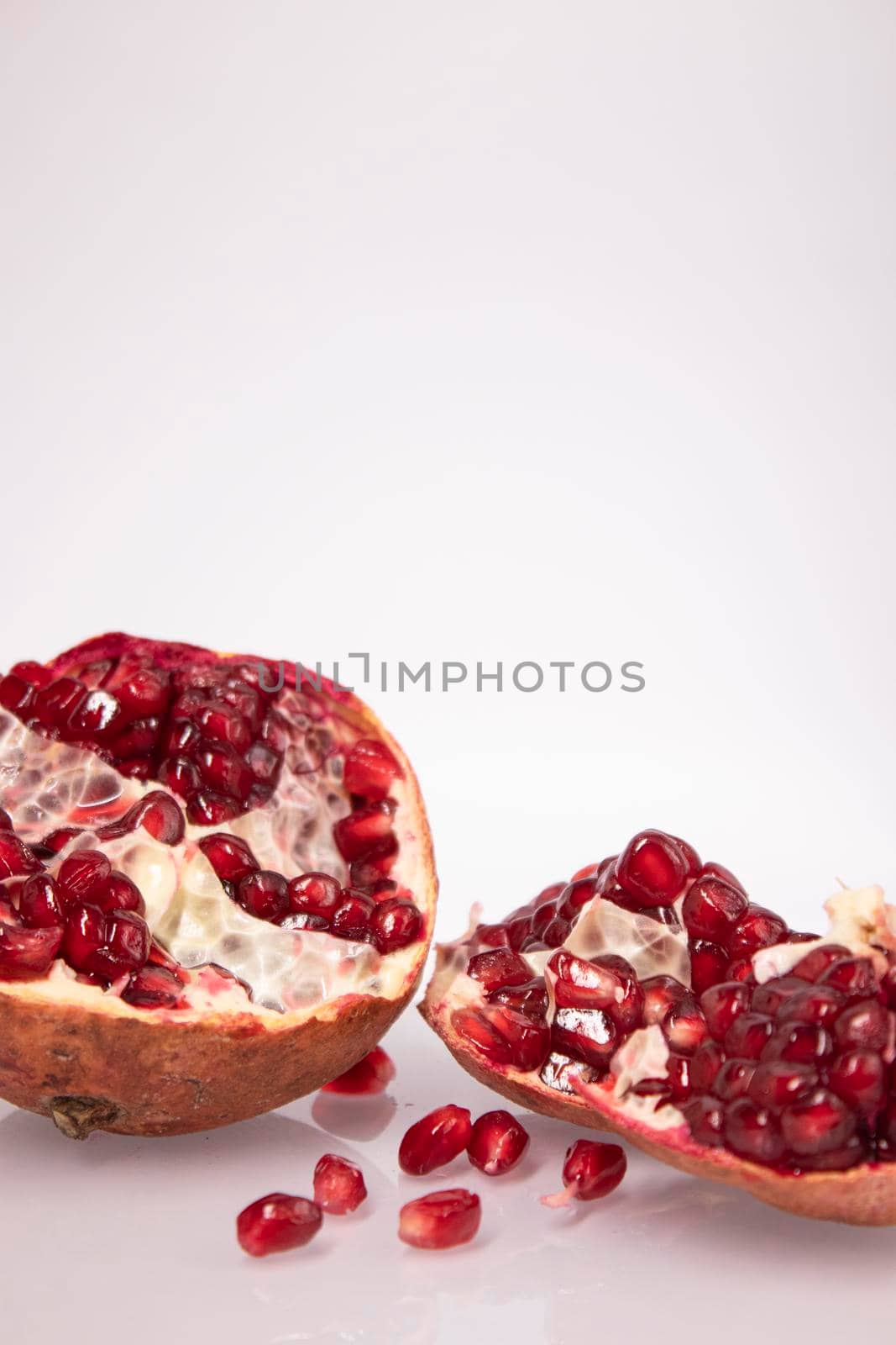 Fresh ripe sliced pomegranate fruit with red seeds isolated on white background by oliavesna