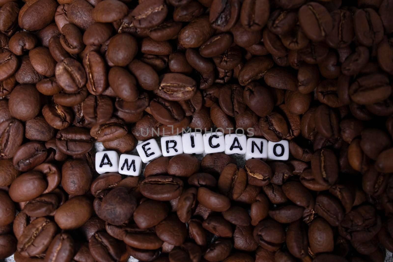 close up of Freshly roasted coffee beans near word AMERICANO written with little white cubes. top view.