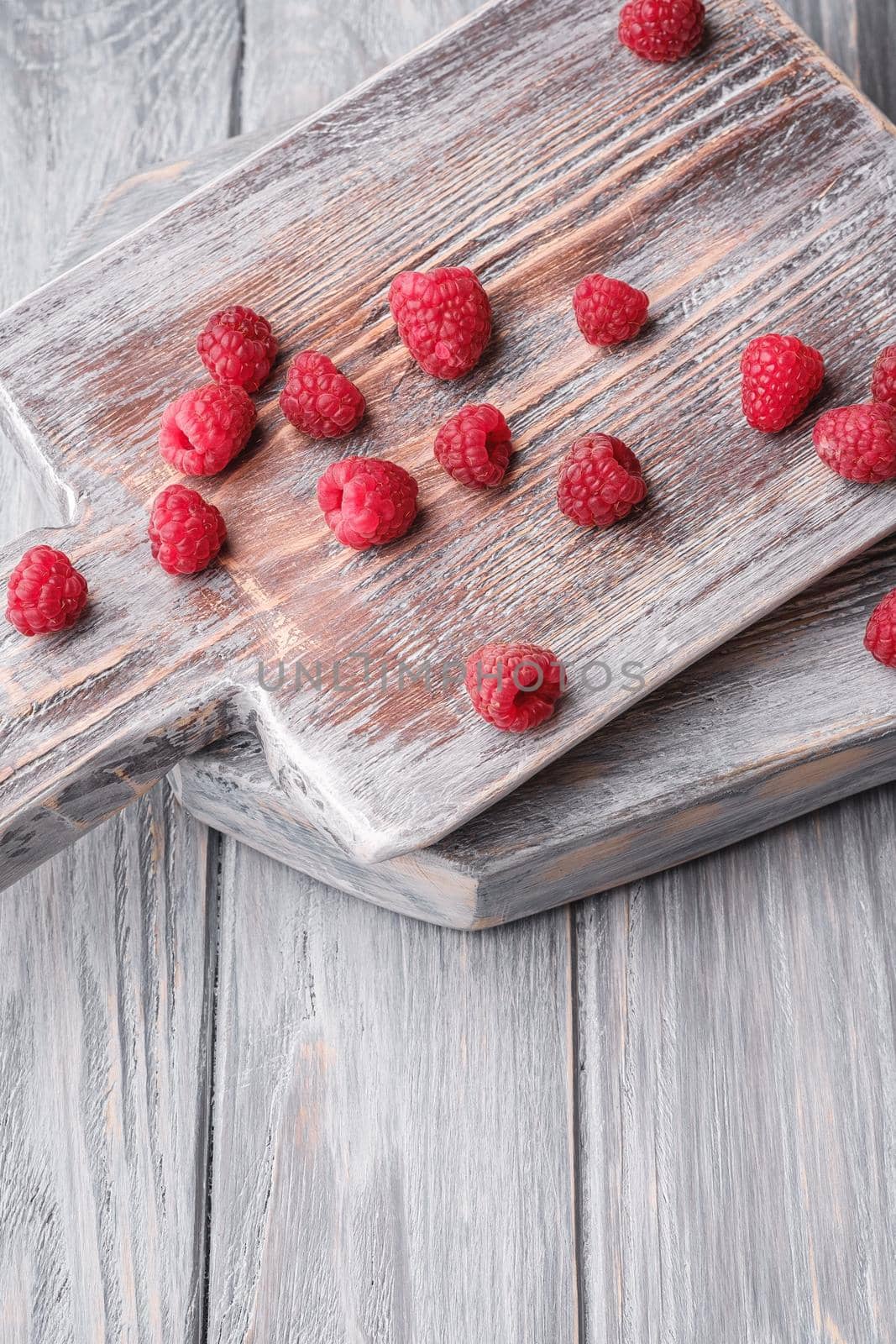 Raspberry fruits on old cutting board, healthy pile of summer berries on grey wooden background, angle view by Frostroomhead