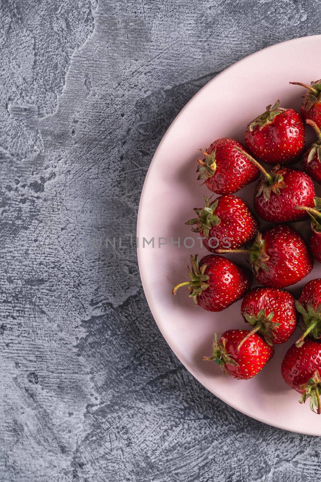 Fresh ripe strawberry fruits in pink plate, summer vitamin berries on grey stone background, top view