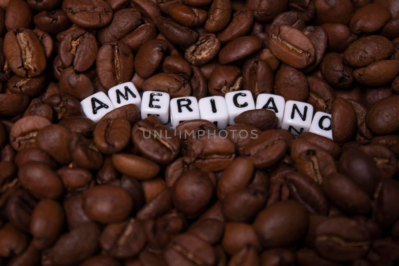 close up of Freshly roasted coffee beans near word AMERICANO written with little white cubes. top view.