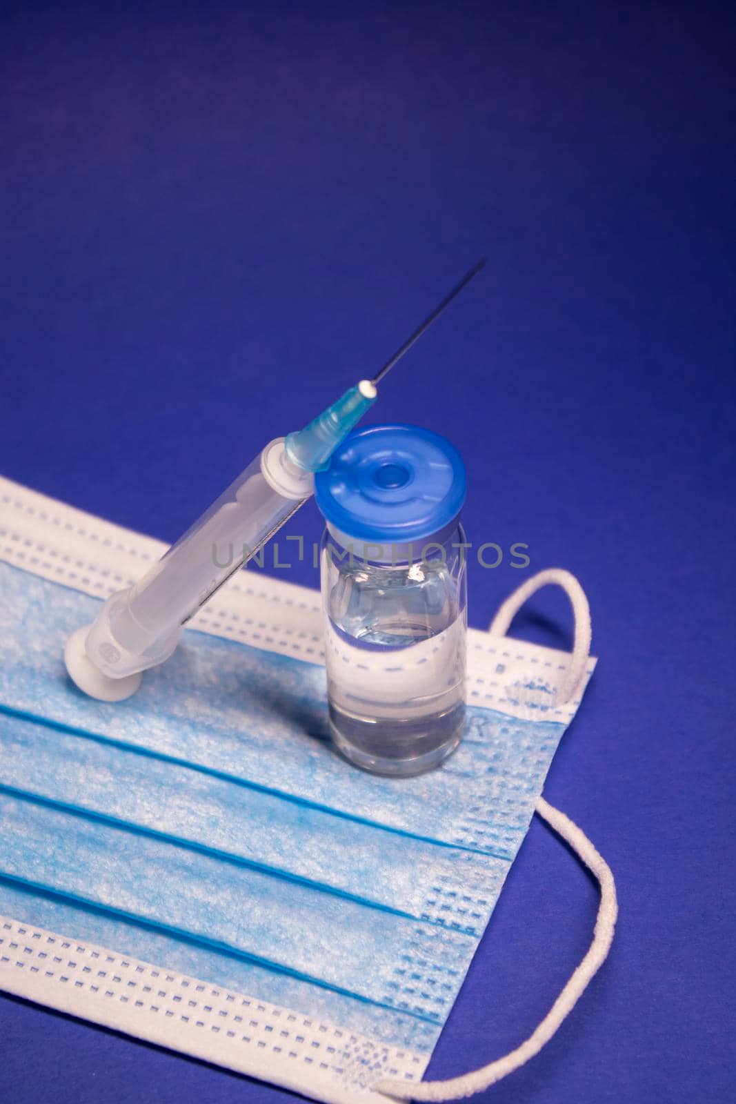 Vaccine bottle phial with no label on blue medical mask and medical syringe with injection needle. isolated on blue background. cure. Development of coronavirus vaccine COVID-19. by oliavesna