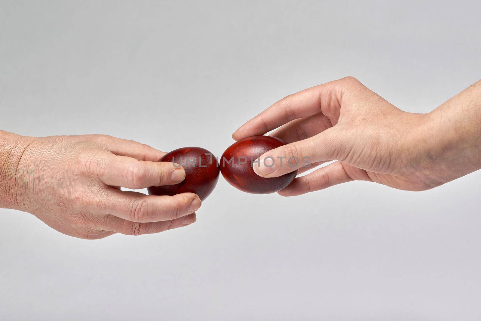 Two hands holding Easter eggs check their strength on a light background. Beat the easter eggs
