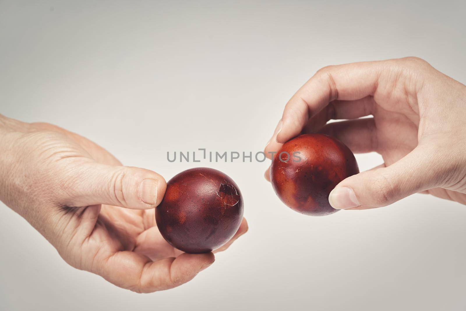 Two hands holding Easter eggs check their strength on a light background. Beat the easter eggs