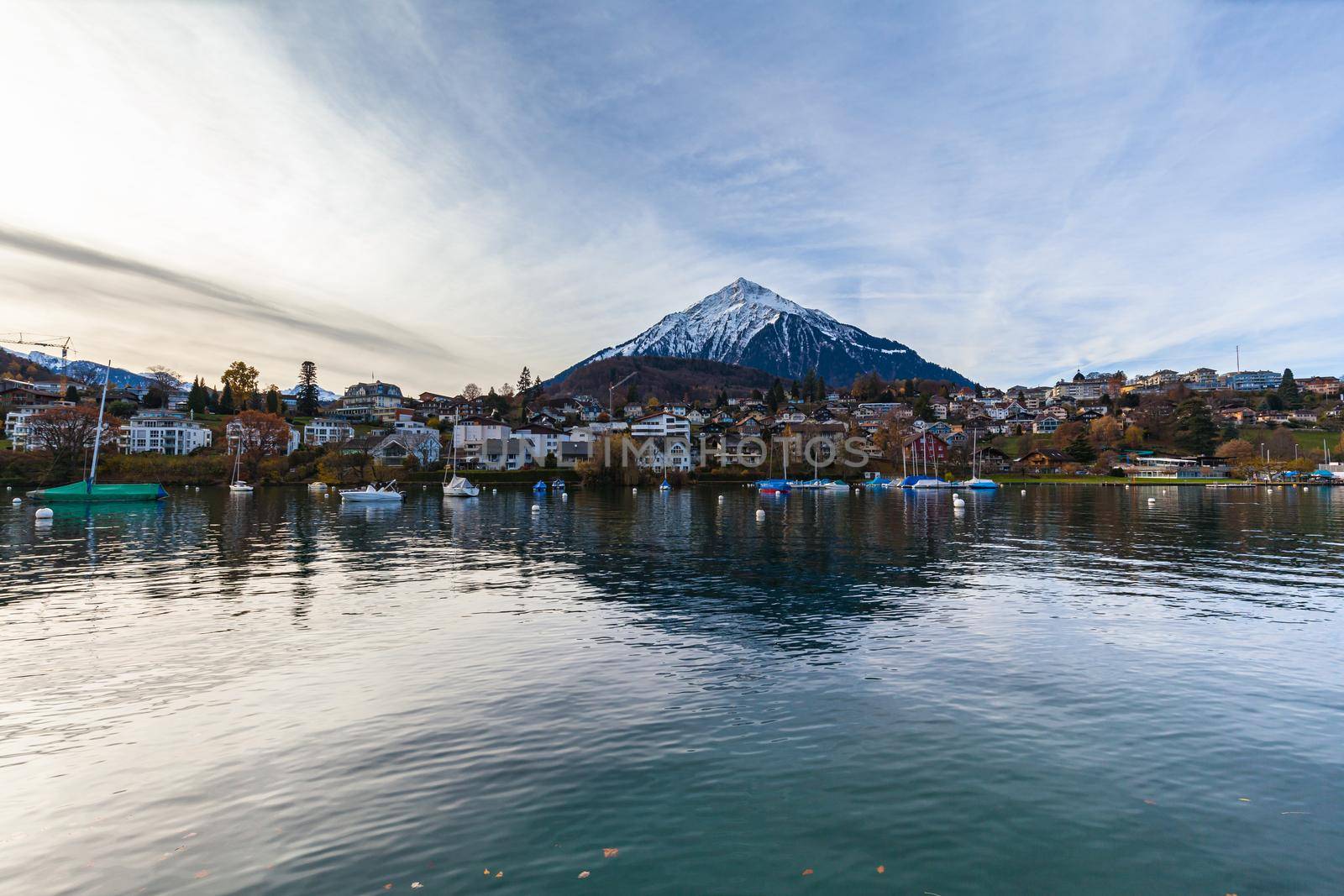 Stunning panorama view of the Spiez village with the snow covered Niederhorn of Swiss Alps on Bernese Oberland in background, from side of Lake Thun on a cloudy autumn day, Spiez, Bern, Switzerland