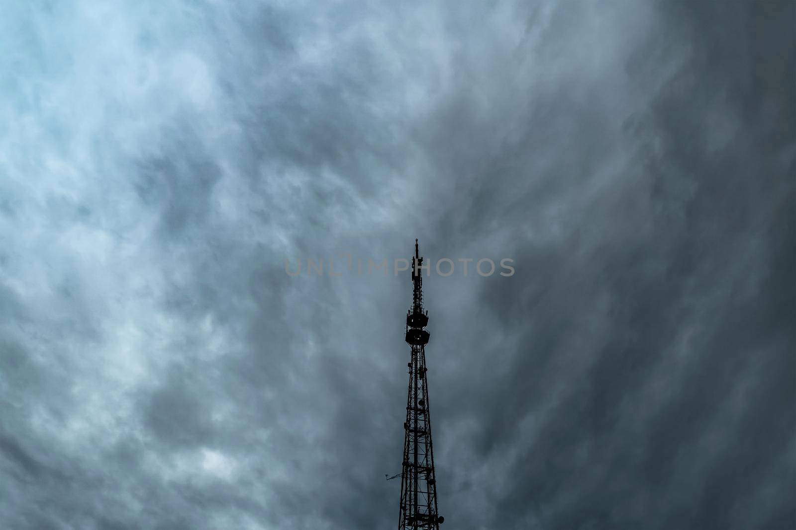 A television or radio broadcasting antenna against a dramatic overcast sky.A cloudy sky with thick rain clouds and a telephone antenna.Communications and telecommunications.Connect and wireless media