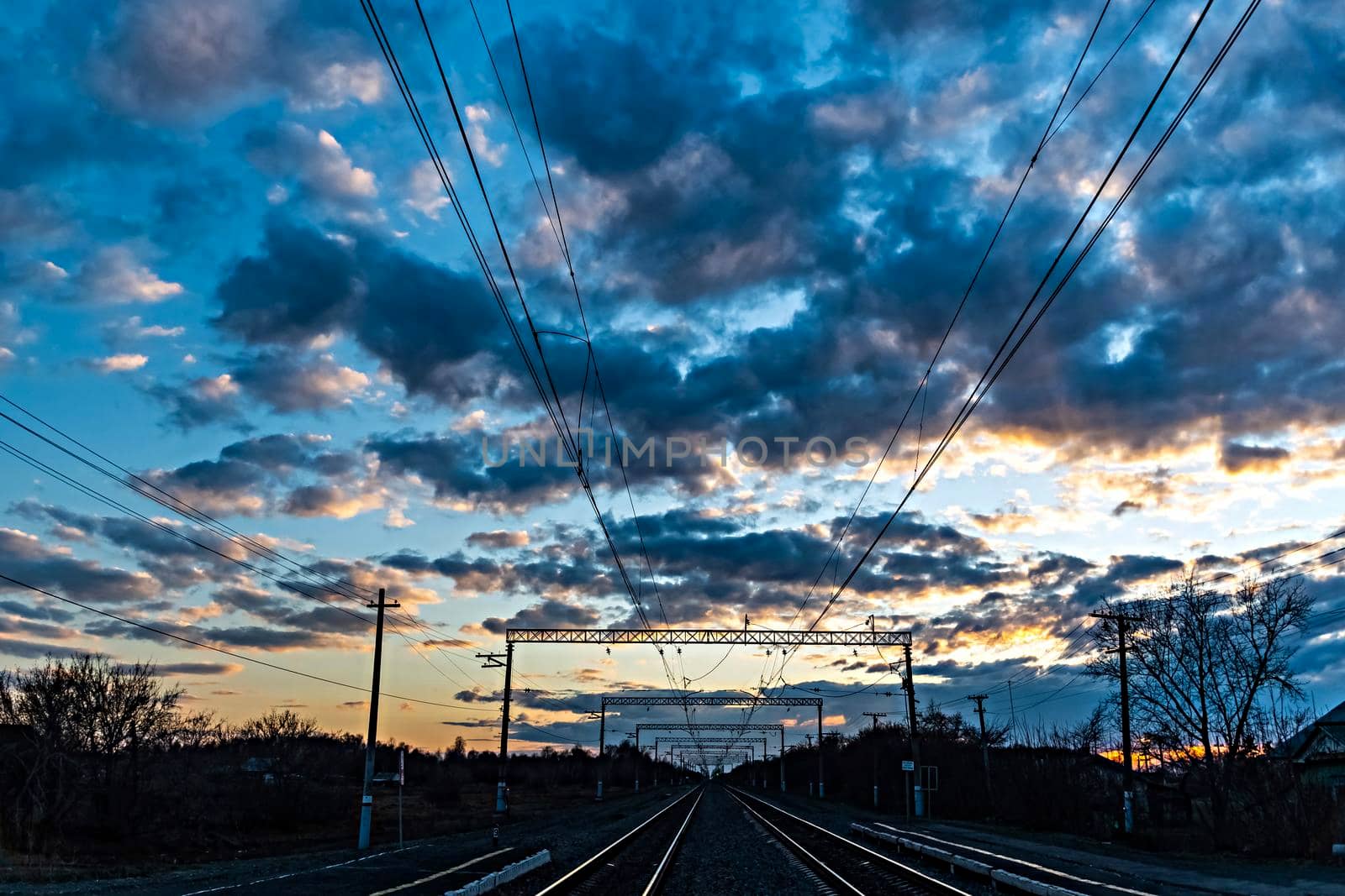 A railway with railway tracks, poles and wires at the dawn of the sun.The heavenly light of the sun.Dramatic evening sky with clouds and rays of the sun.Sunlight at evening sunset or morning dawn.View