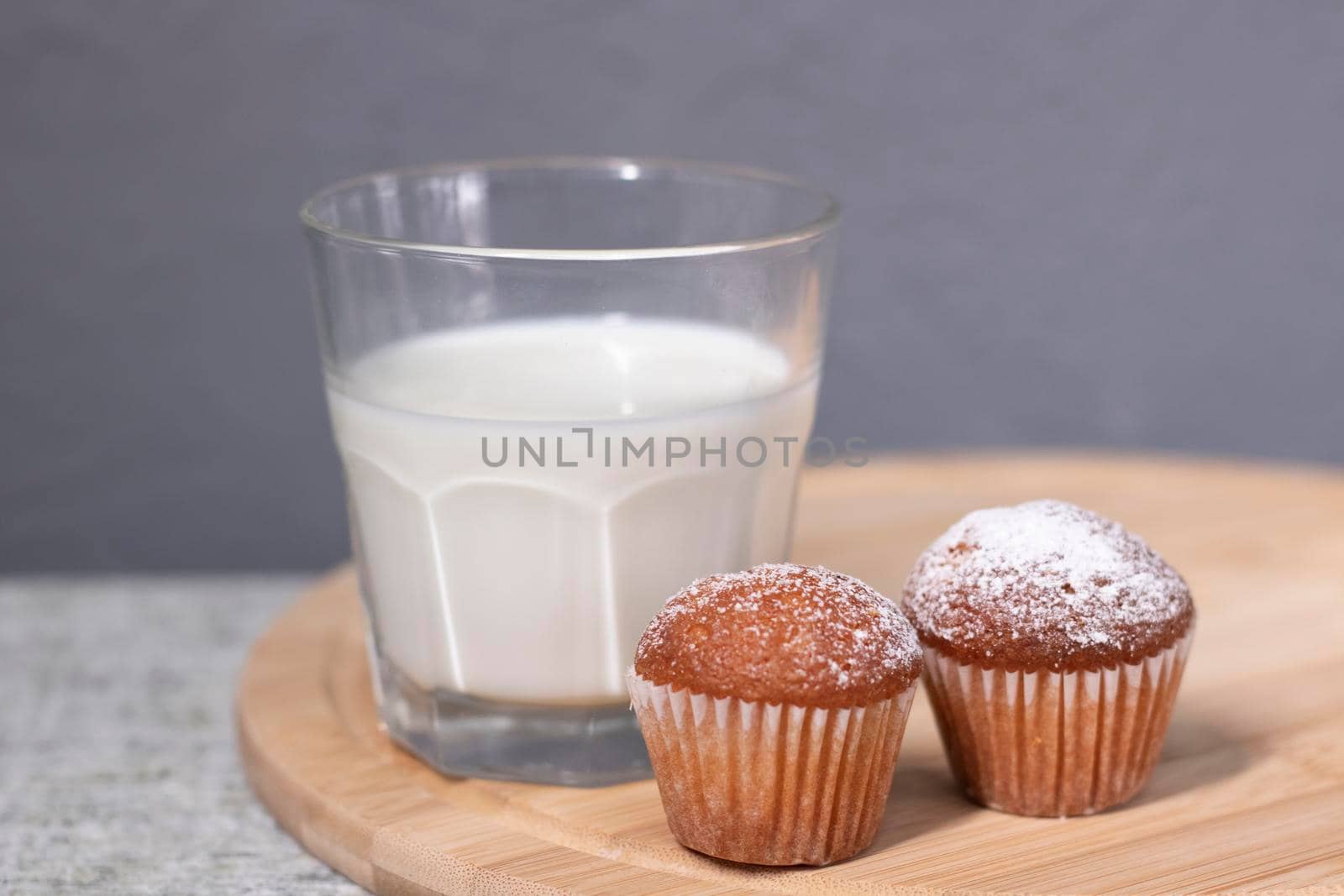 two little cupcakes or muffins in powdered sugar near a glass of milk. healthy breakfast. snack or lunch.