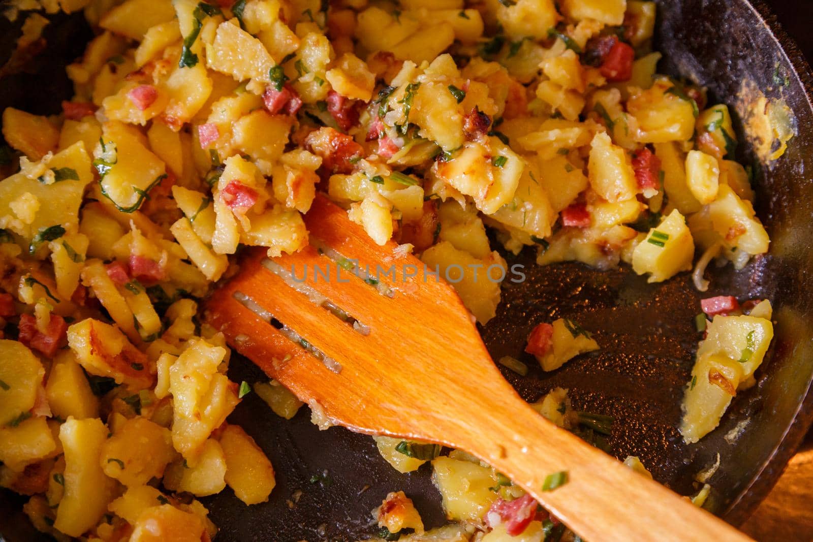 roasted domestic potatos in a frying pan with wooden spatula close-up with selective focus.