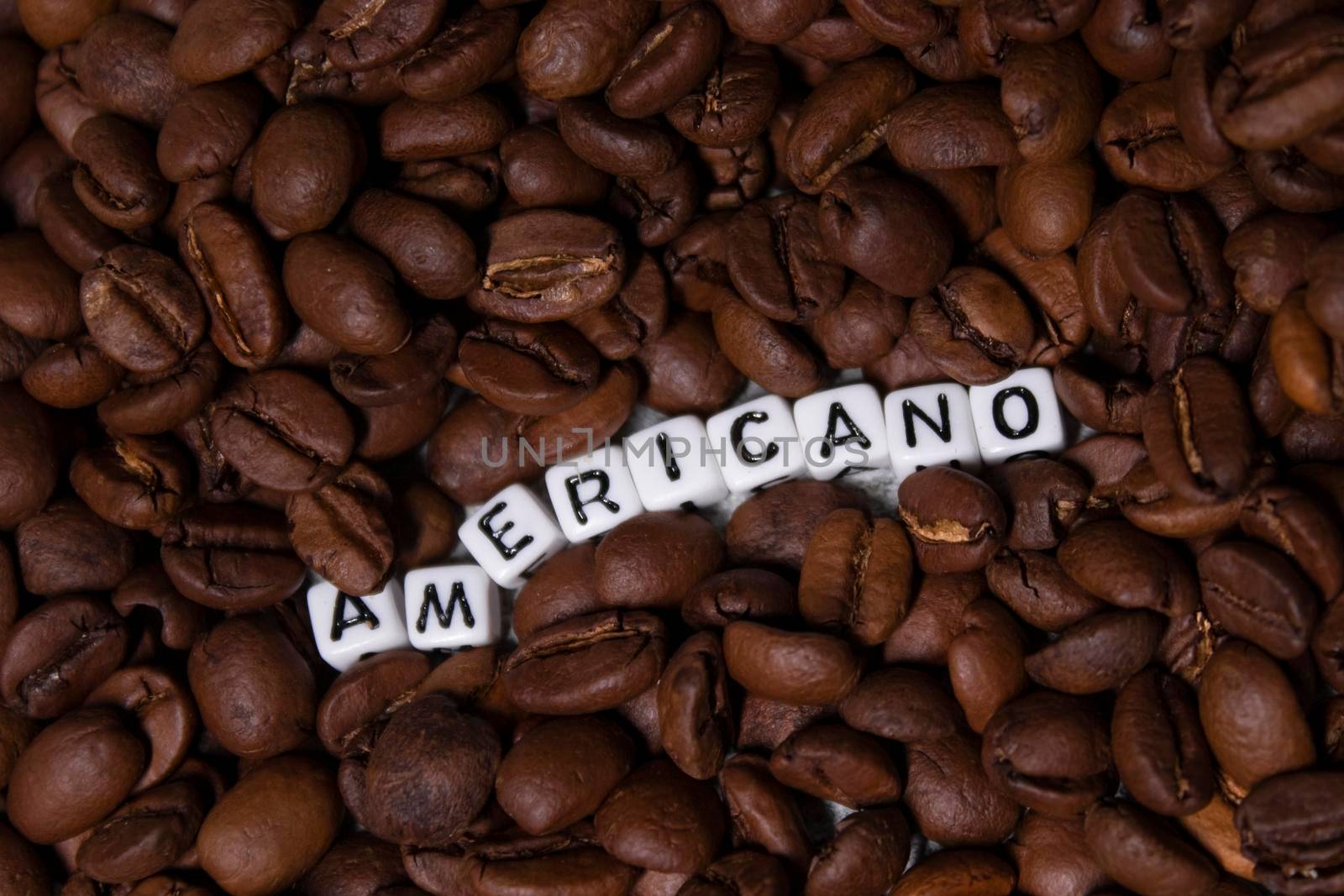 close up of Freshly roasted coffee beans near word AMERICANO written with little white cubes. top view.