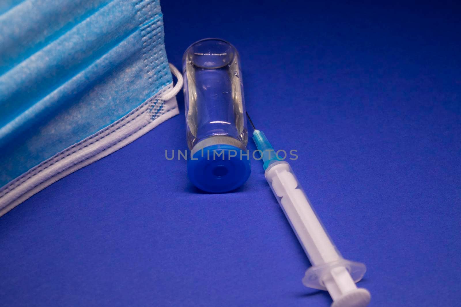 Vaccine bottle phial with no label near blue medical mask and medical syringe with injection needle. isolated on blue background. cure. Development of coronavirus vaccine COVID-19. copy space