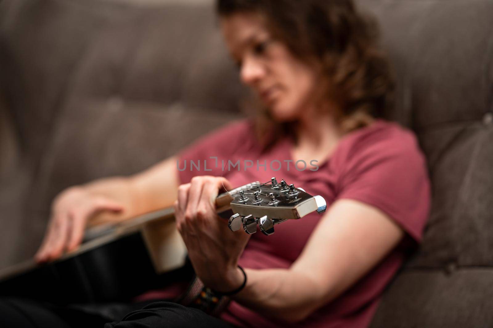 woman playing guitar at home on the couch.