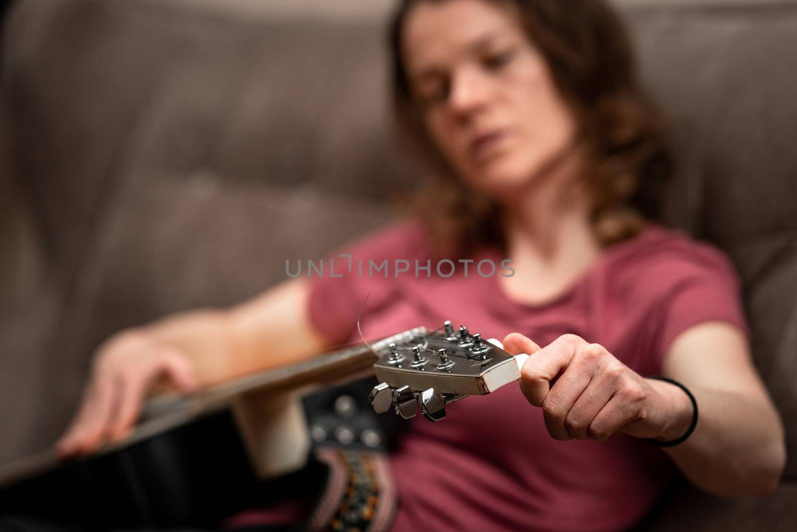 woman tuning guitar at home on the couch by Edophoto