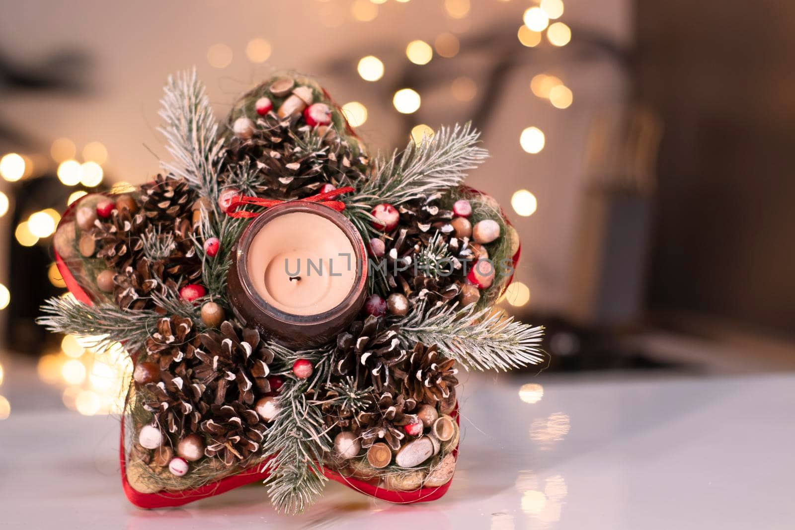 Christmas decor star-shaped made of tree branch with new years toys on it and a candle in it.