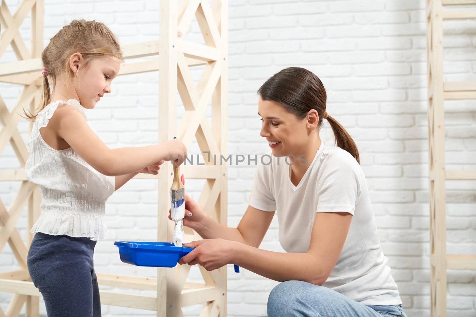 Smiling mother and daughter painting wooden rack. by SerhiiBobyk
