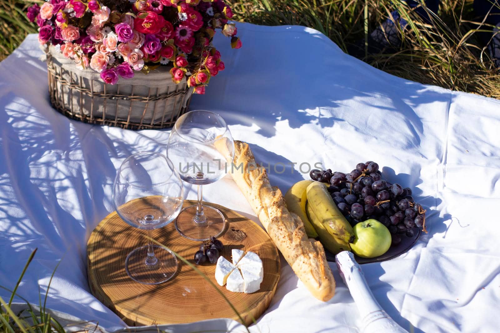 wooden stand with two glasses of champagne, grapes, baguette and camembert cheese on white blanket in the field. picnic by oliavesna