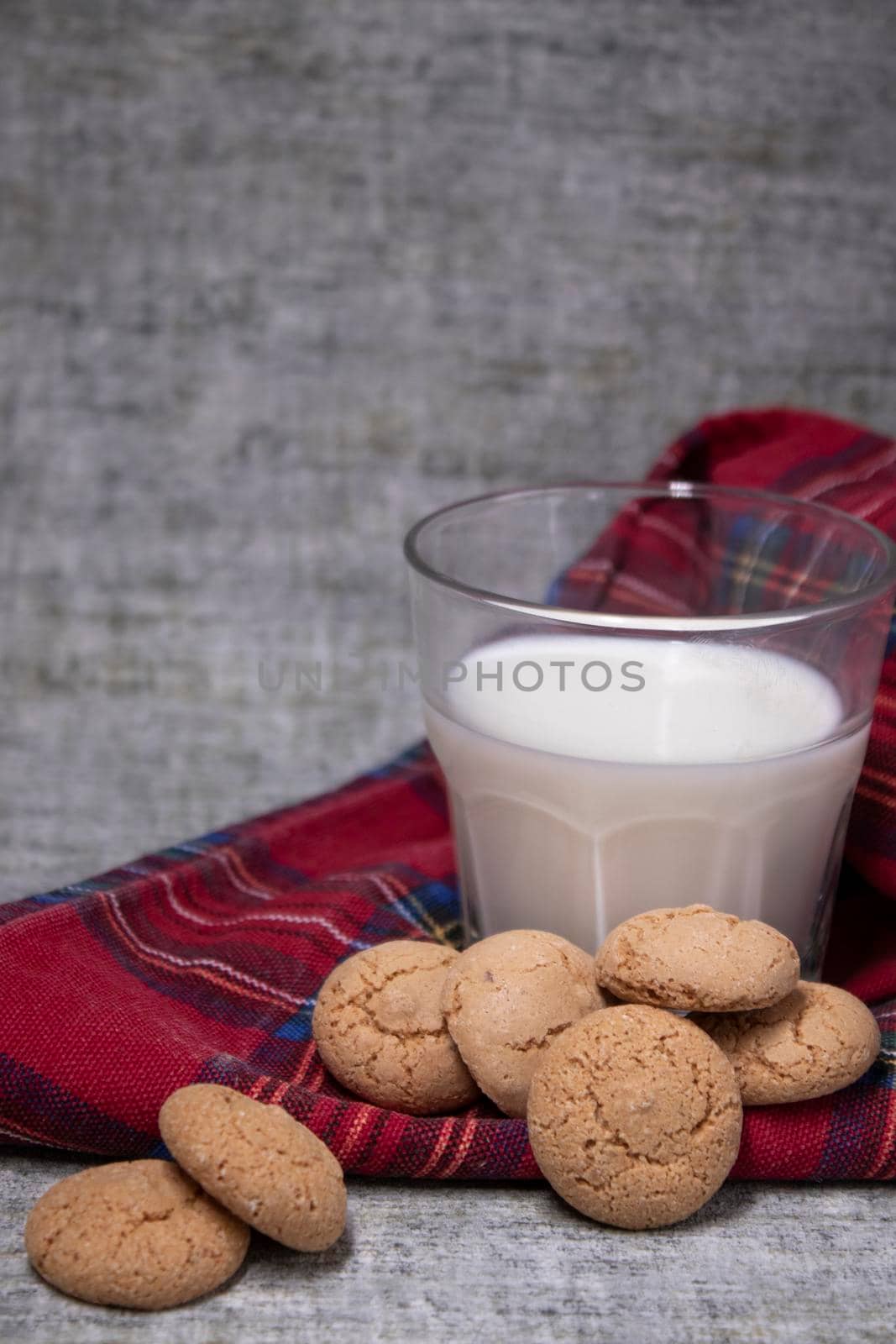 glass of milk near almond amaretti cookies on plaid red fabric tablecloth. healthy breakfast snack.