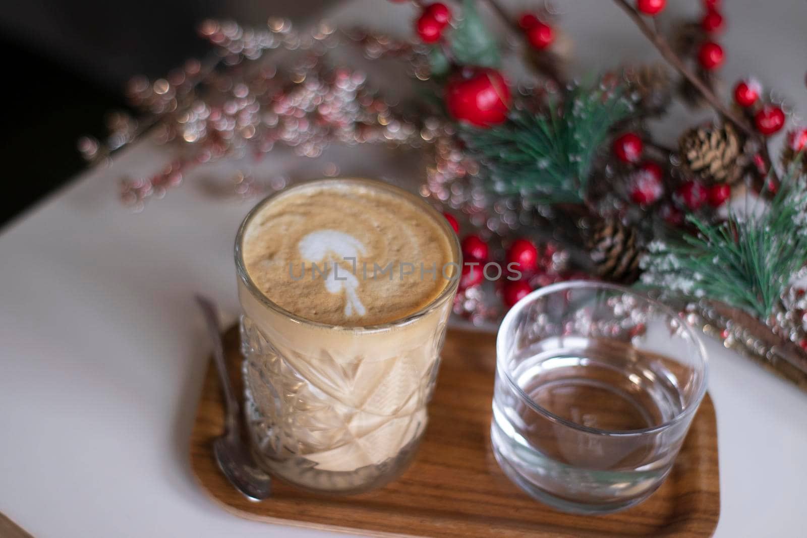 cup of coffee latte or cappuccino with a glass of water on a tray. near decorative red branches. interior, cozy copy space