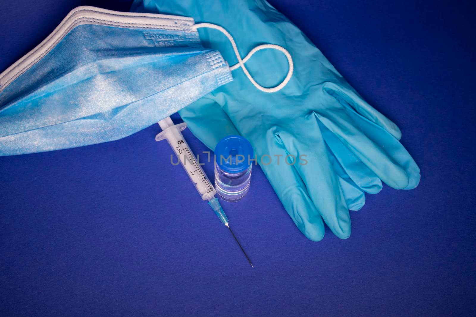 Vaccine bottle phial with no label, medical syringe with injection needle, blue medical mask and gloves . isolated on blue background. cure. Development of coronavirus vaccine COVID-19 by oliavesna