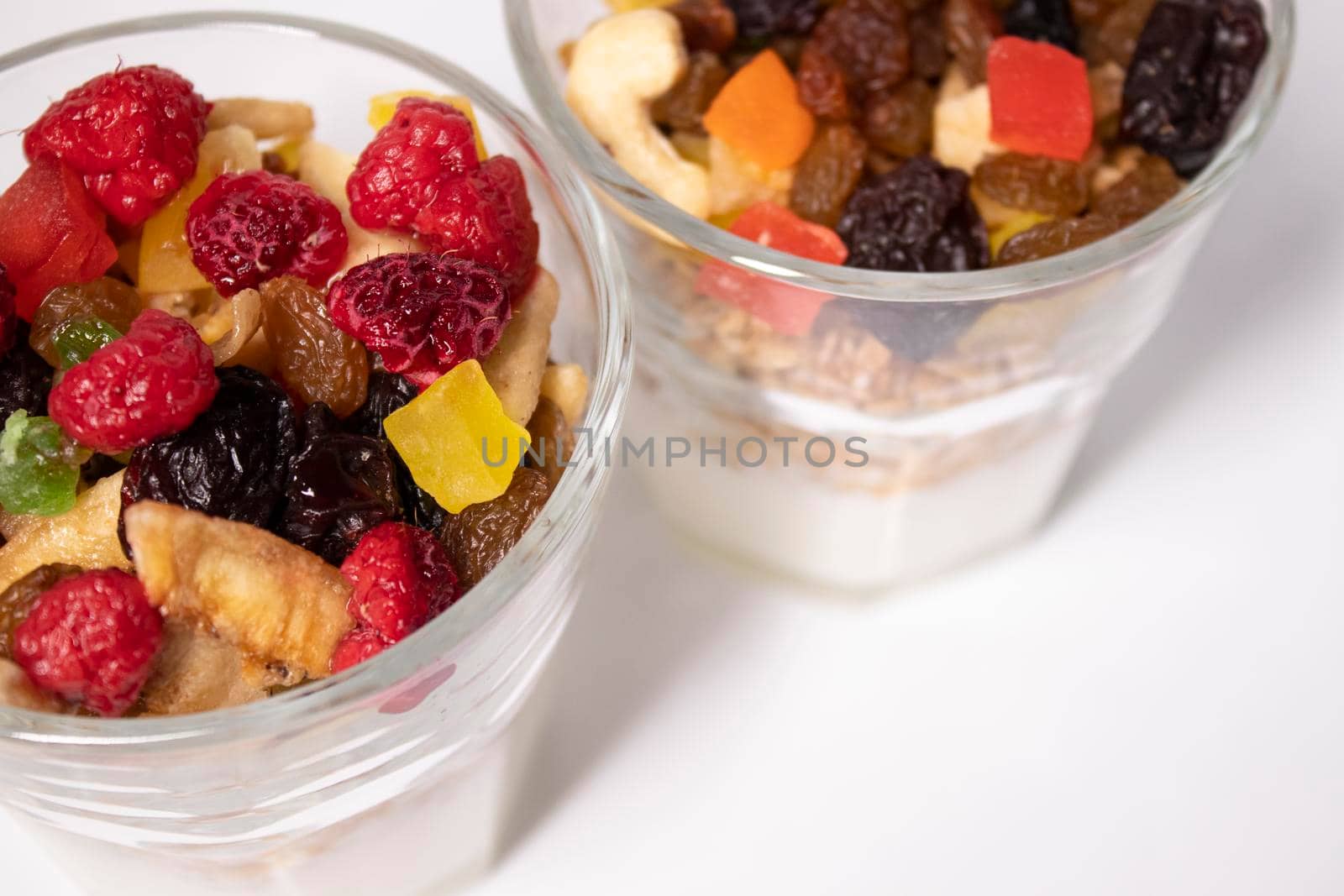 muesli dessert with yogurt and candied or dried fruits with raspberries on top in glass isolated on white background. Granola breakfast by oliavesna