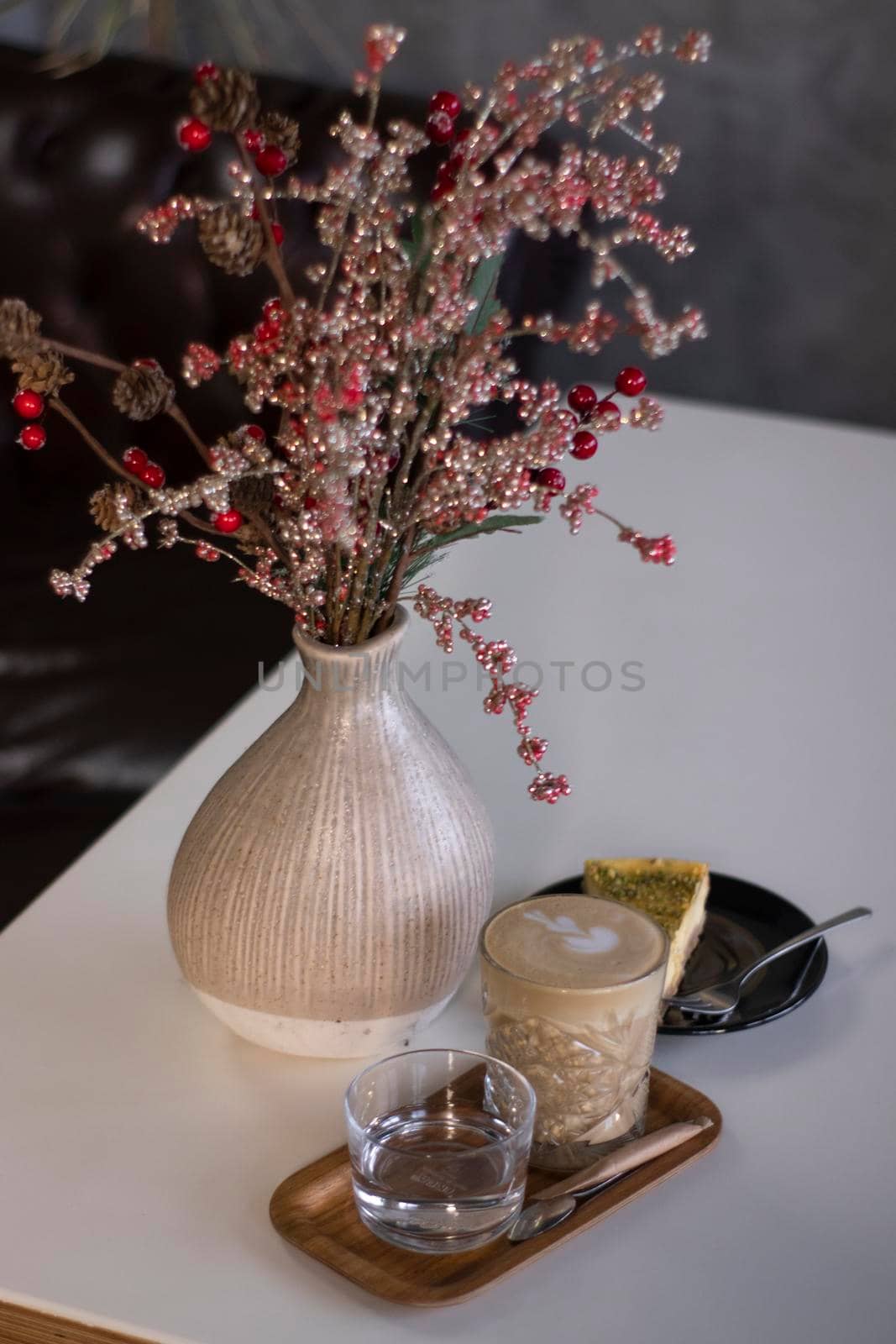 cup of coffee latte or cappuccino with piece of cake near vase with decorative red branches. interior, cozy. copy space