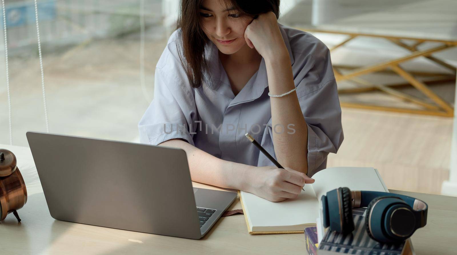 Online education. Asian girl taking note for online lesson using a computer video call to a virtual teacher at home by nateemee