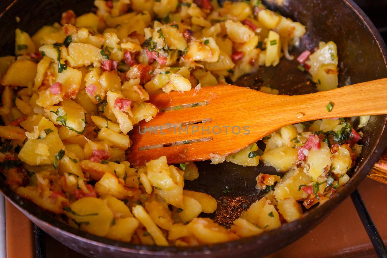 roasted domestic potatos in a frying pan with wooden spatula close-up with selective focus.
