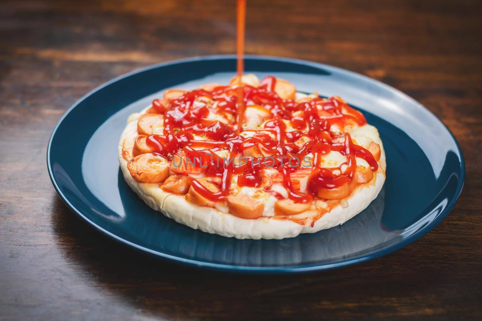 Put tomato sauce on the pizza, sausage and crab sticks in a ceramic plate on a wooden table.