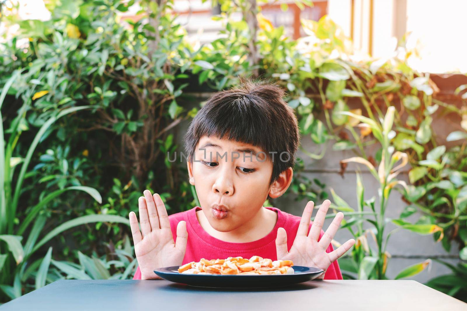 Cute Asian child in a red shirt showed a good expression when he saw a pizza in a plate placed in front of the table.