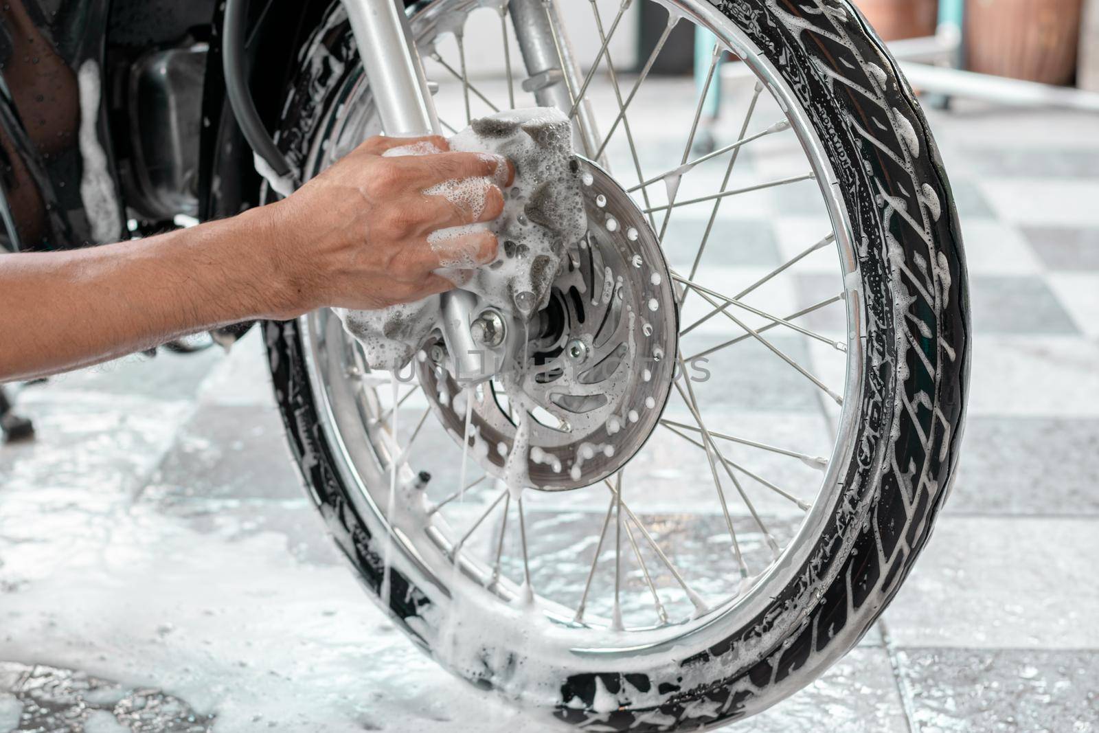 Close-up of a man's hand washing a motorbike's wheels with sponges and bubbles.