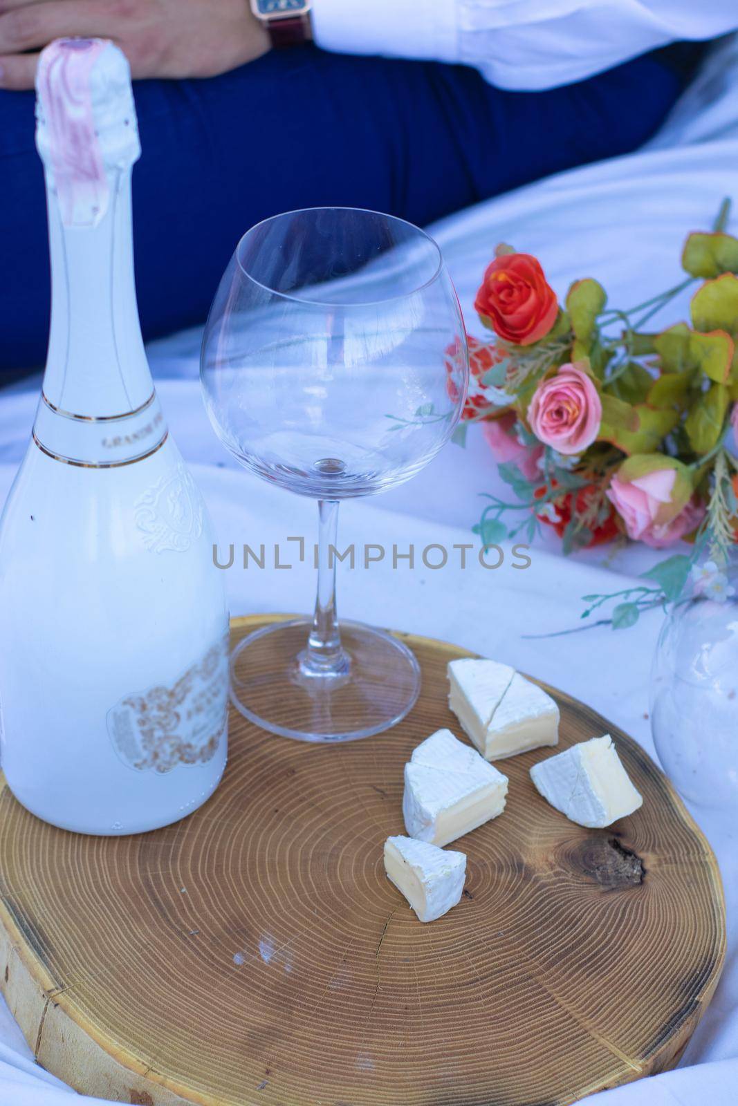 wooden stand with one glass of champagne and a bottle and camembert cheese on a white blanket in the field. picnic by oliavesna