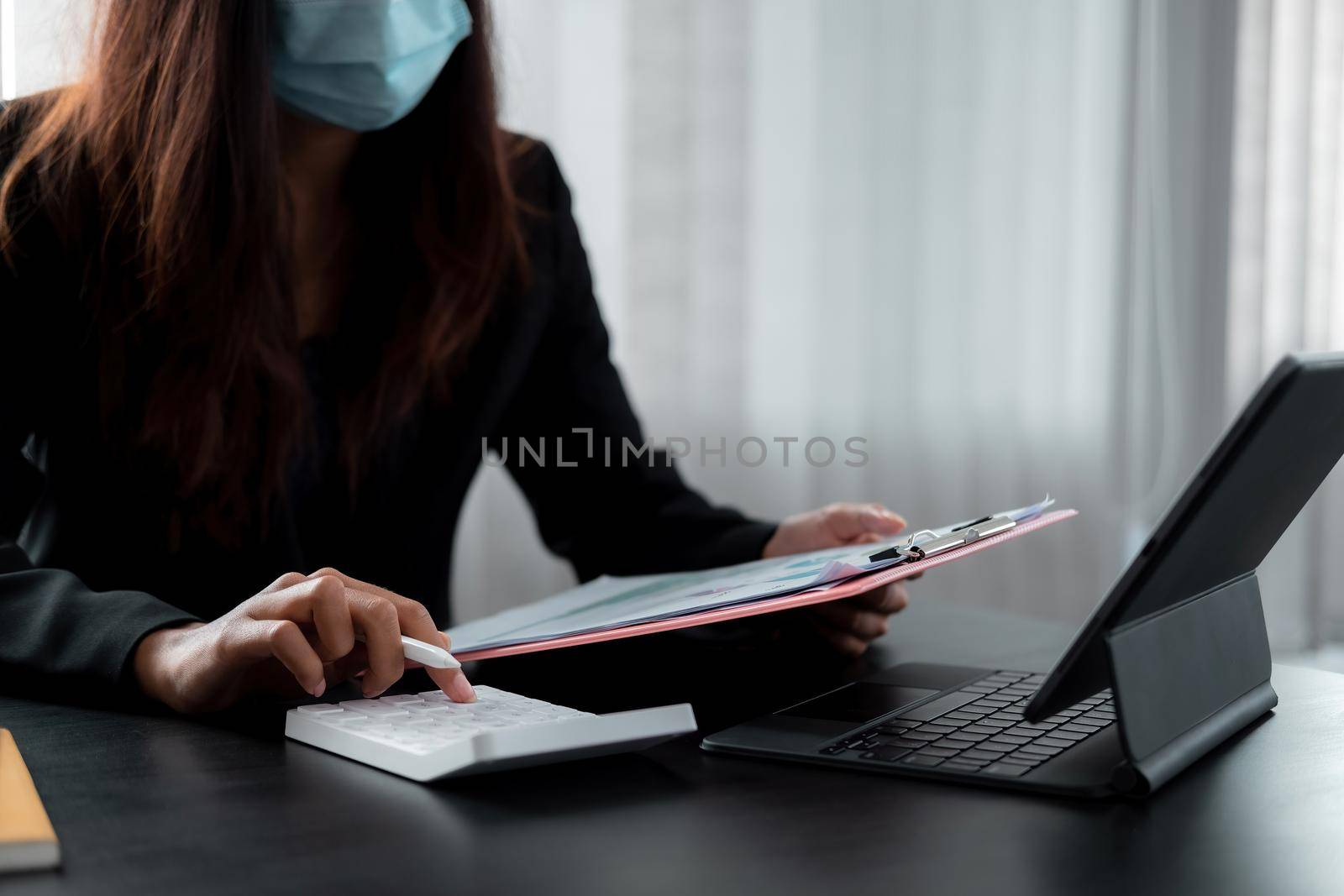 businesswoman wear mask working on desk office with using a calculator to calculate the numbers, finance accounting concept