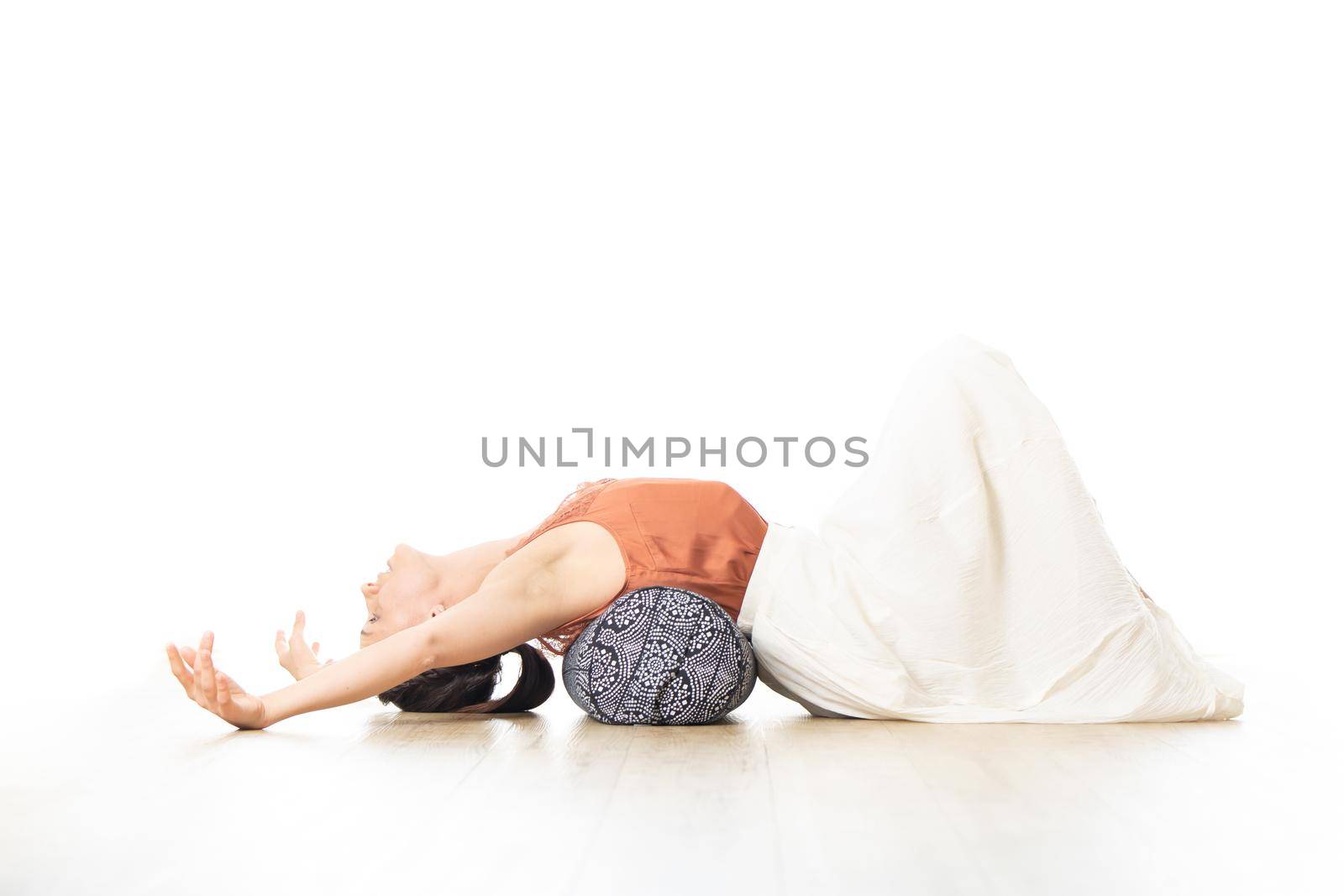 Restorative yoga with a bolster. Young sporty attractive woman in bright white yoga studio, stretching and relaxing during restorative yoga with bolster cushion. Healthy active lifestyle.