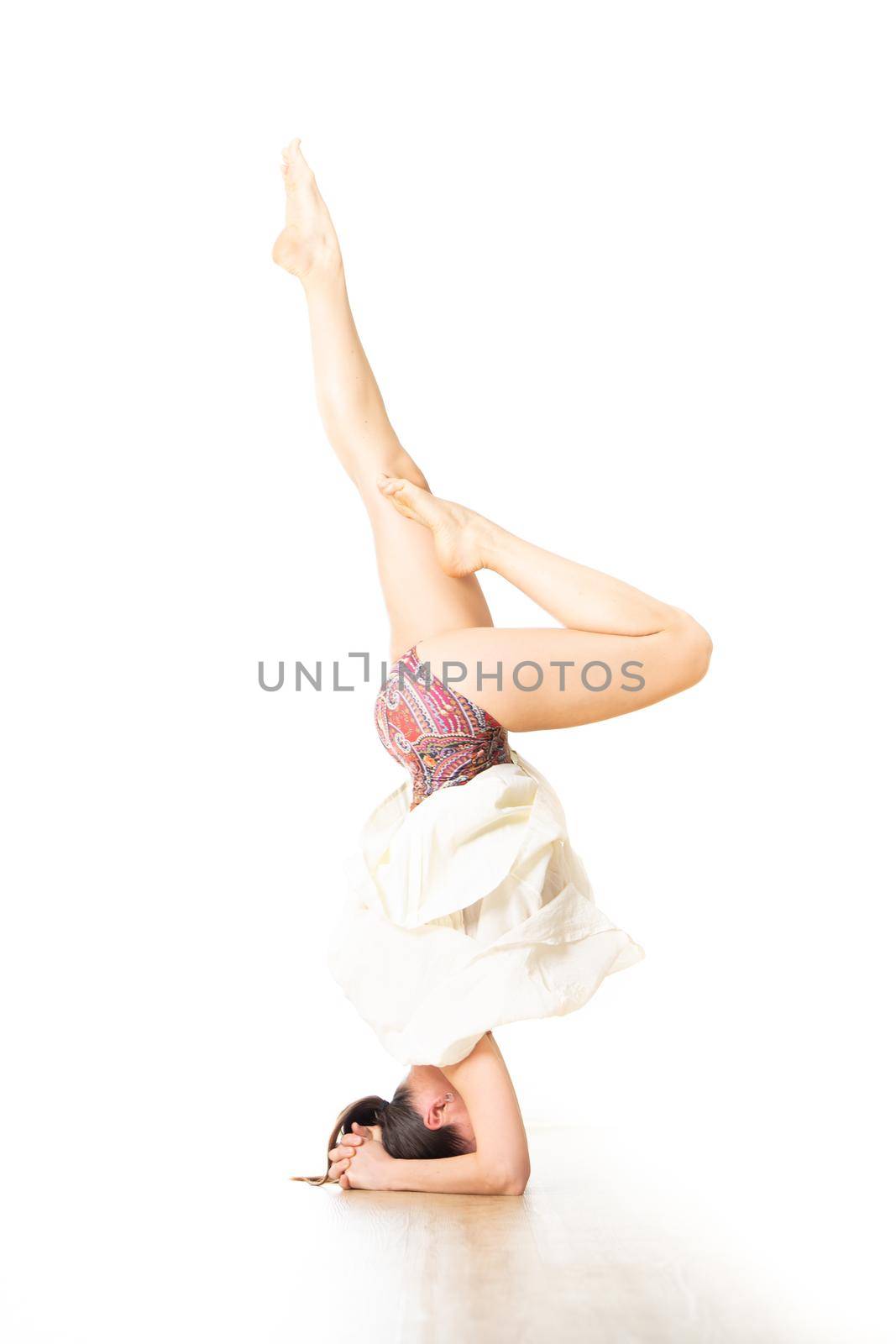 Portrait of active sporty young woman performing standing on head yoga pose in yoga studio. Healthy active lifestyle.