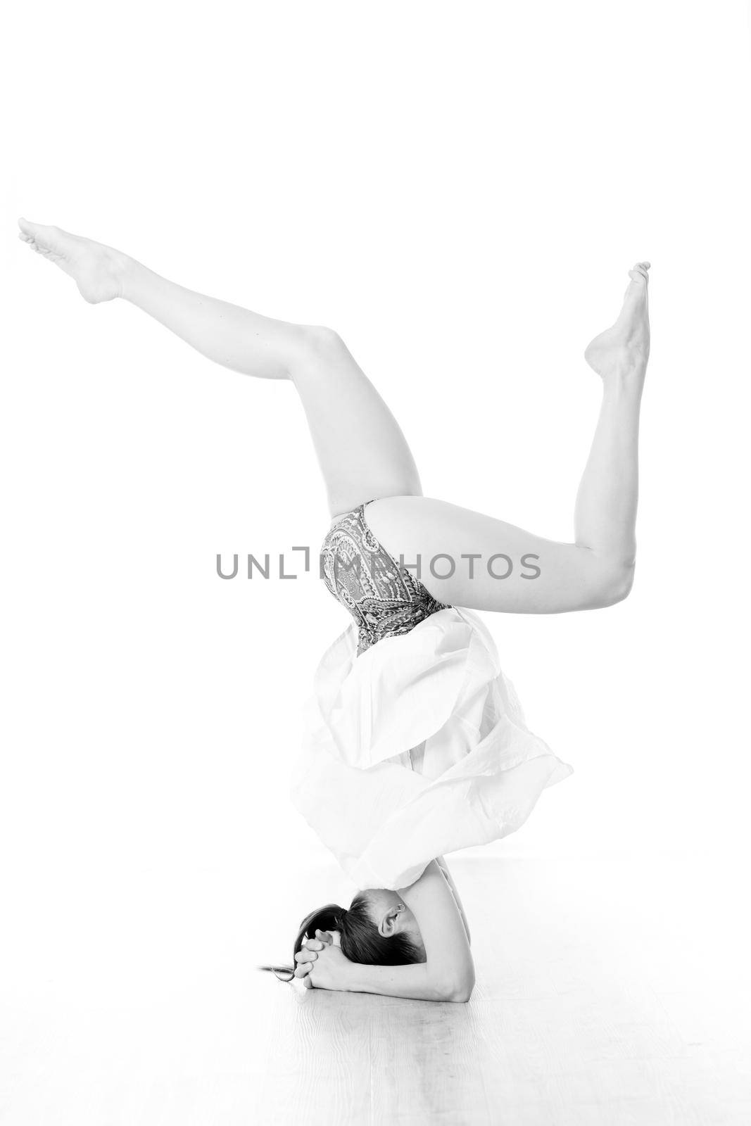 Portrait of beautiful elegant slim active sporty young woman performing standing on head yoga pose in yoga studio. Healthy active lifestyle. Artistic black and white image.