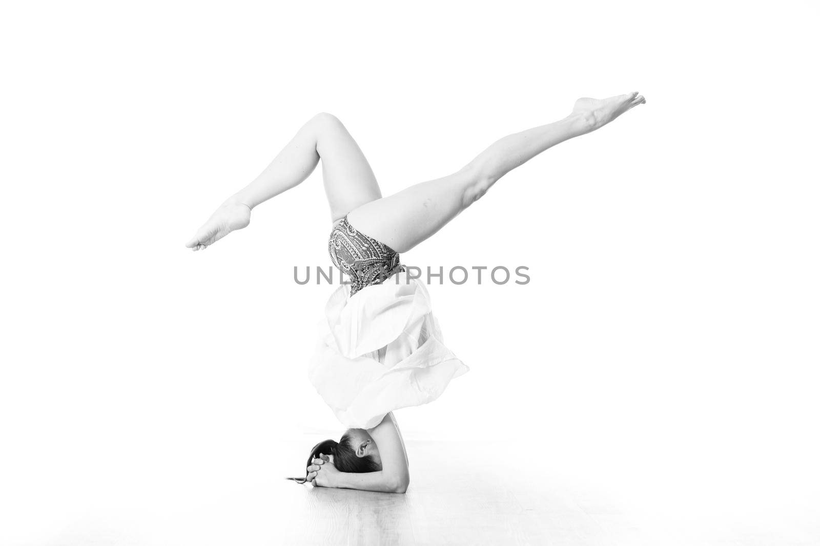 Portrait of beautiful elegant slim active sporty young woman performing standing on head yoga pose in yoga studio. Healthy active lifestyle. Artistic black and white image.