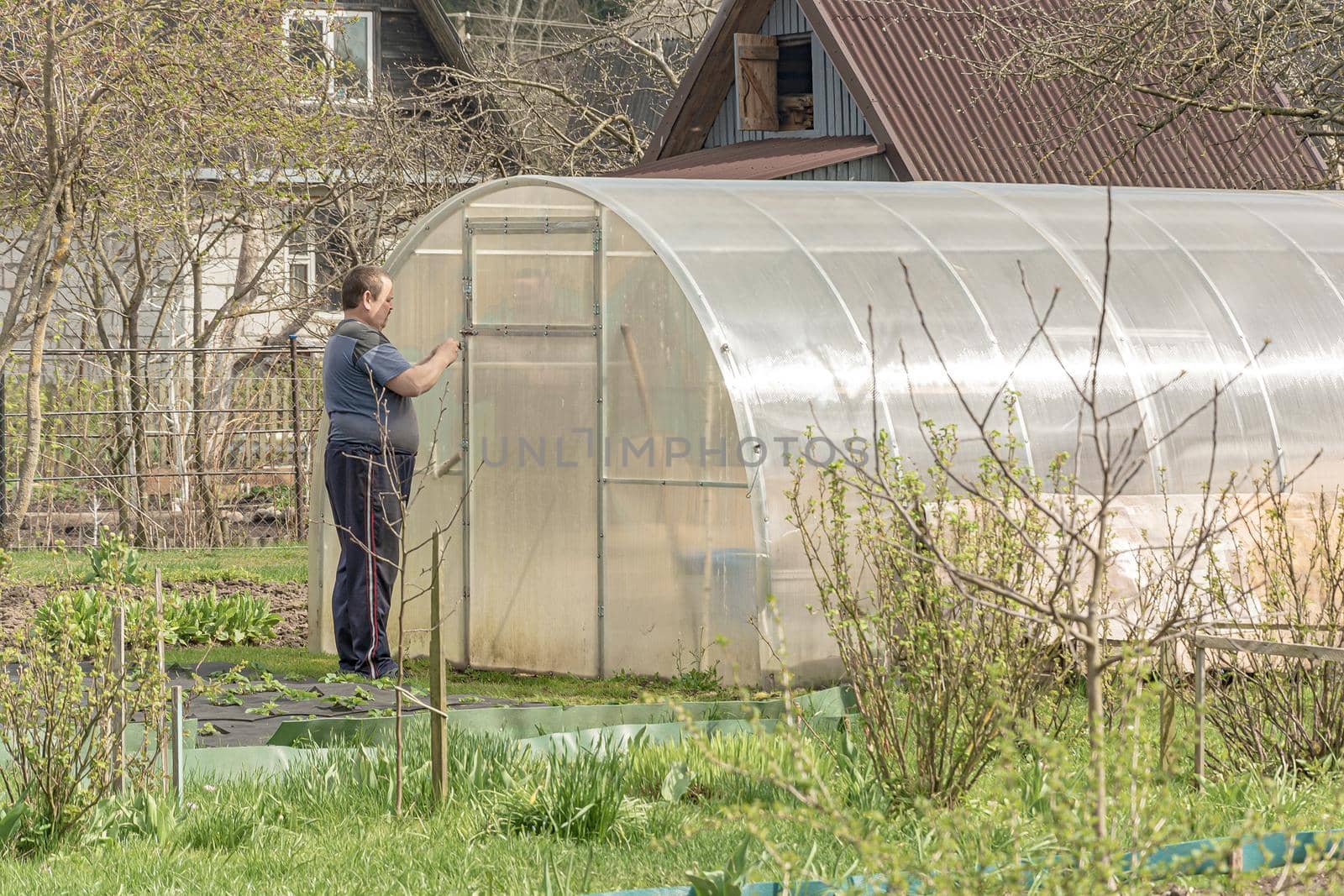 POLAND, Lomza - May 01, 2021: A farmer opens a greenhouse with seedlings on a private farmstead. Stock photo.