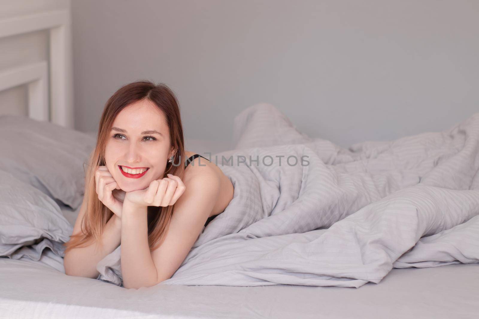 pretty redhead woman in black lace lingerie on bed with grey sheets.