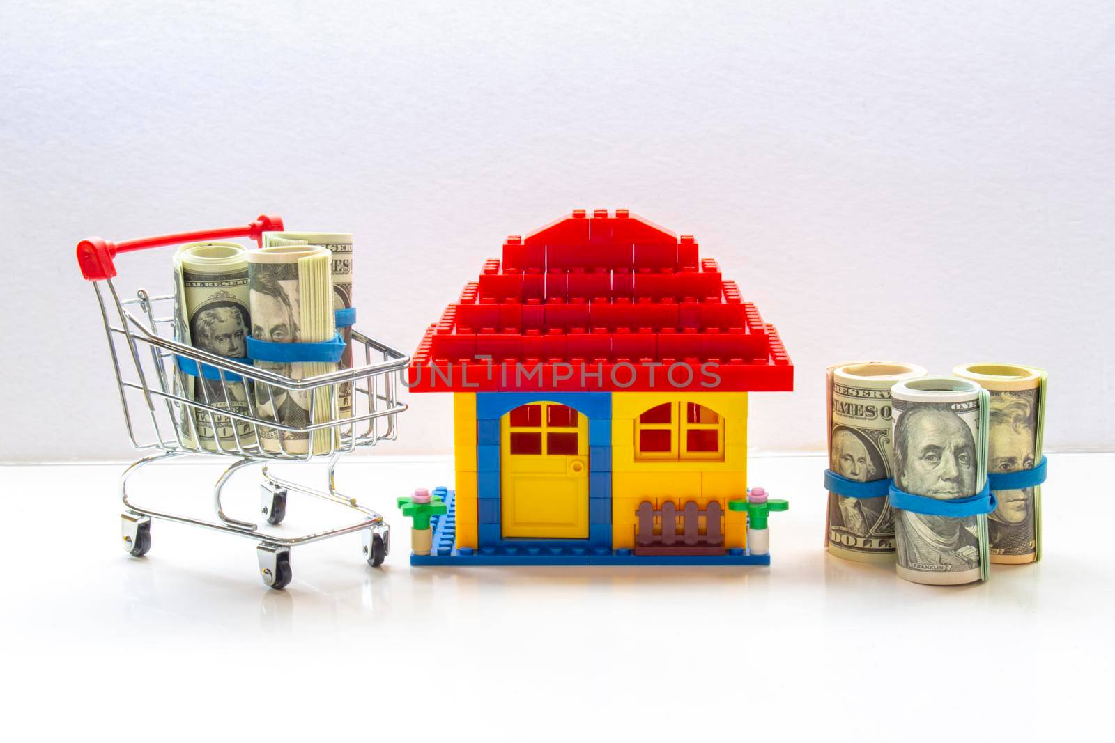 A shopping cart with American USA bank notes bills and a little house on a clear background. Concept: Bank Mortgage