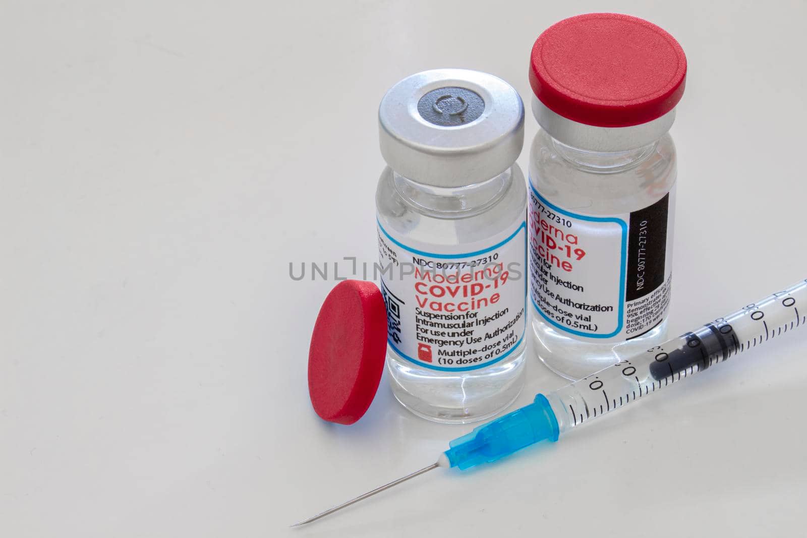 Calgary, Alberta, Canada. April 16, 2021. A couple of Moderna Covid-19 vaccine vials bottles and an injection syringe on a clear table. by oasisamuel